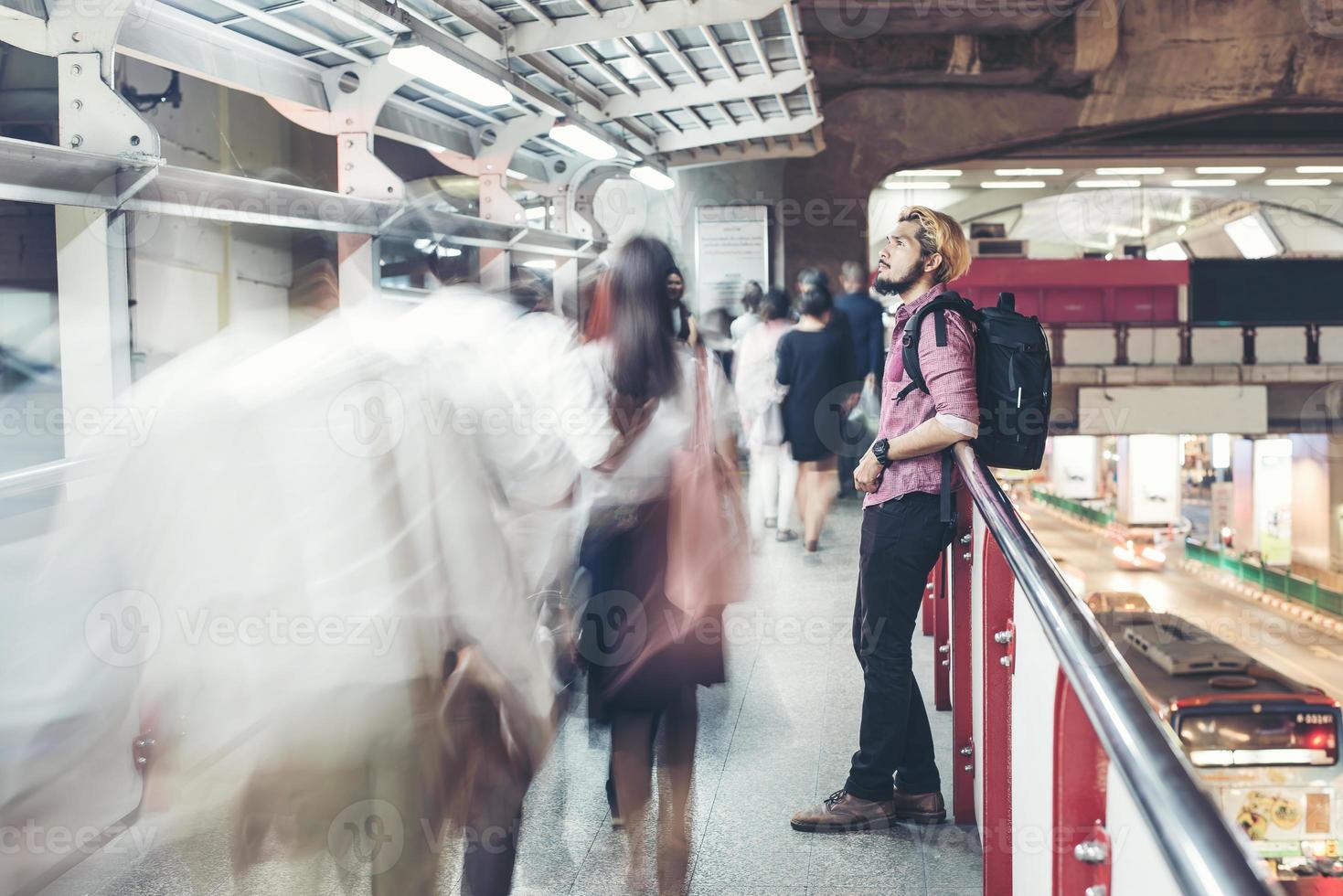 Hipster bearded man standing in the train station with people motion background photo