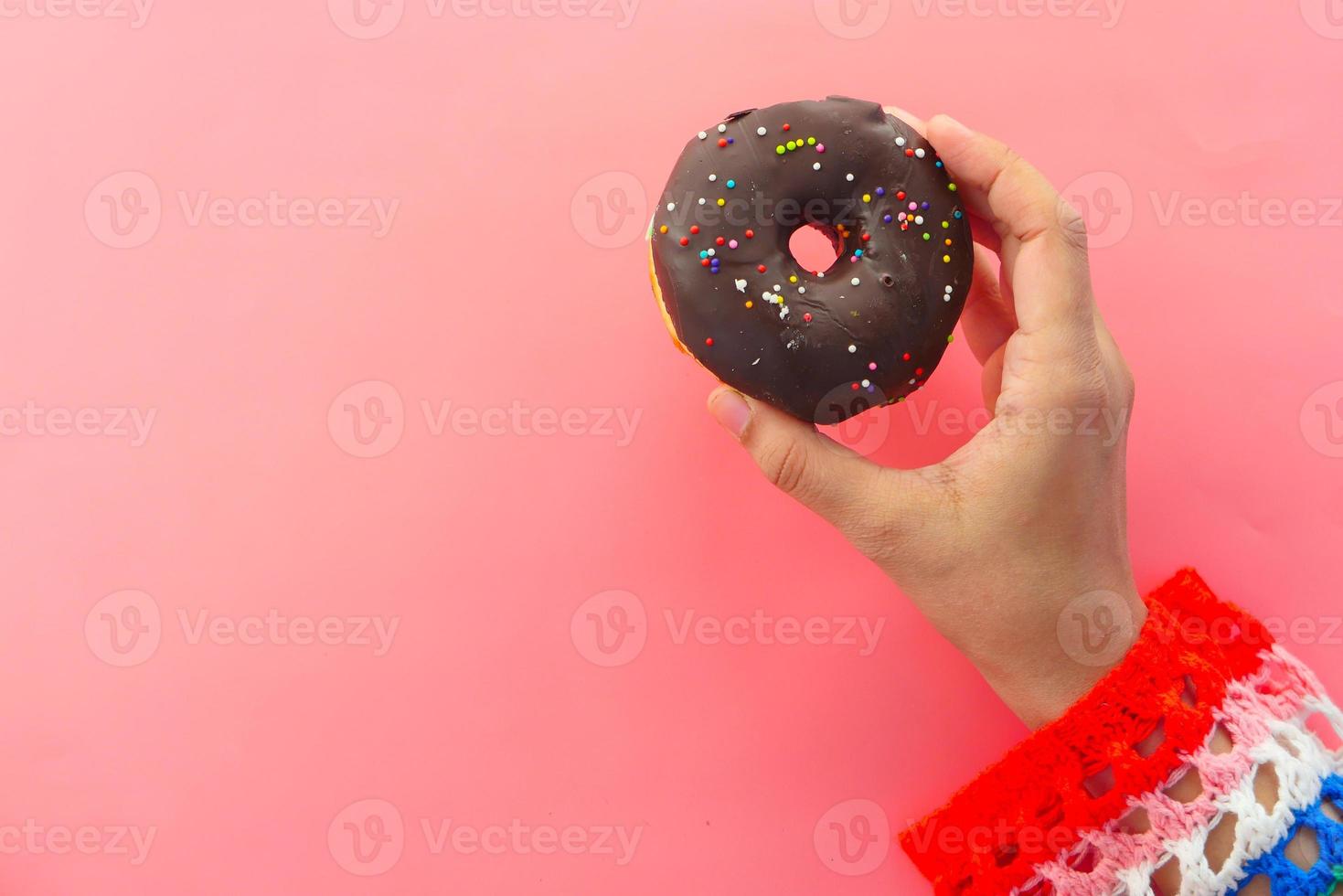 mujer sosteniendo una rosquilla sobre fondo rosa foto