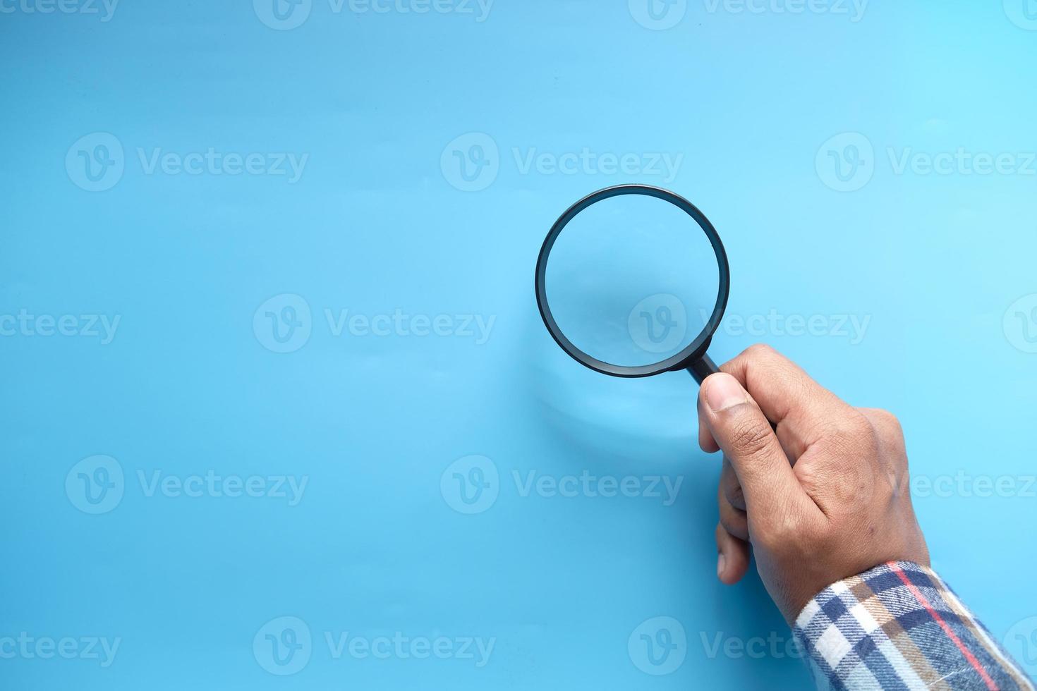 Hand holding a magnifying glass on a blue background photo