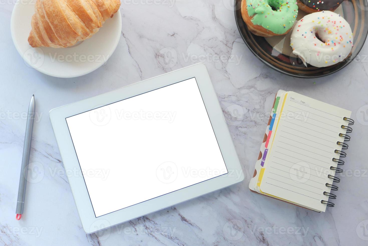 Top view of a tablet with donuts on marble background photo