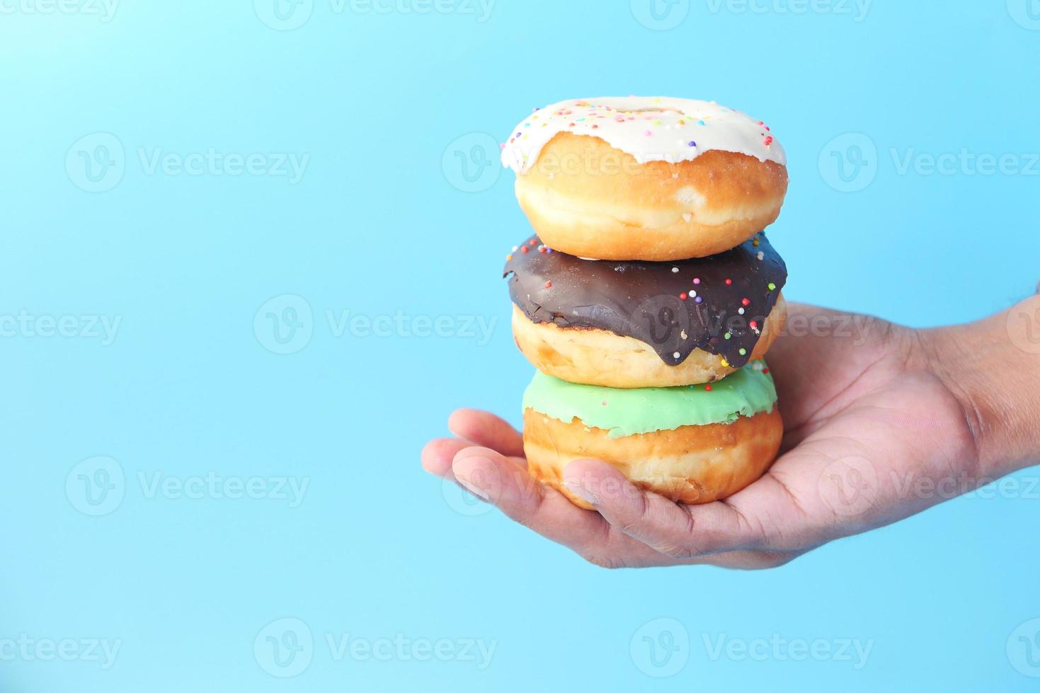 Hombre sujetando donas frescas sobre un fondo azul. foto