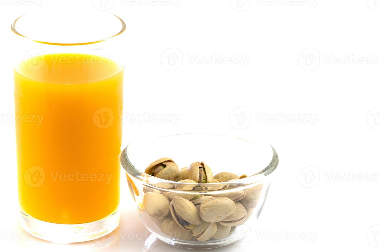 Pistachos en una placa de vidrio y un vaso de jugo de naranja aislado en blanco foto