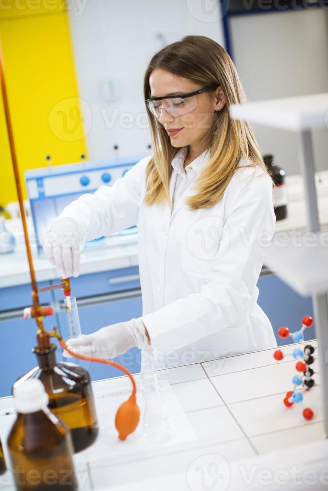 Female researcher standing in the laboratory and analyzing flask with liquid sample photo