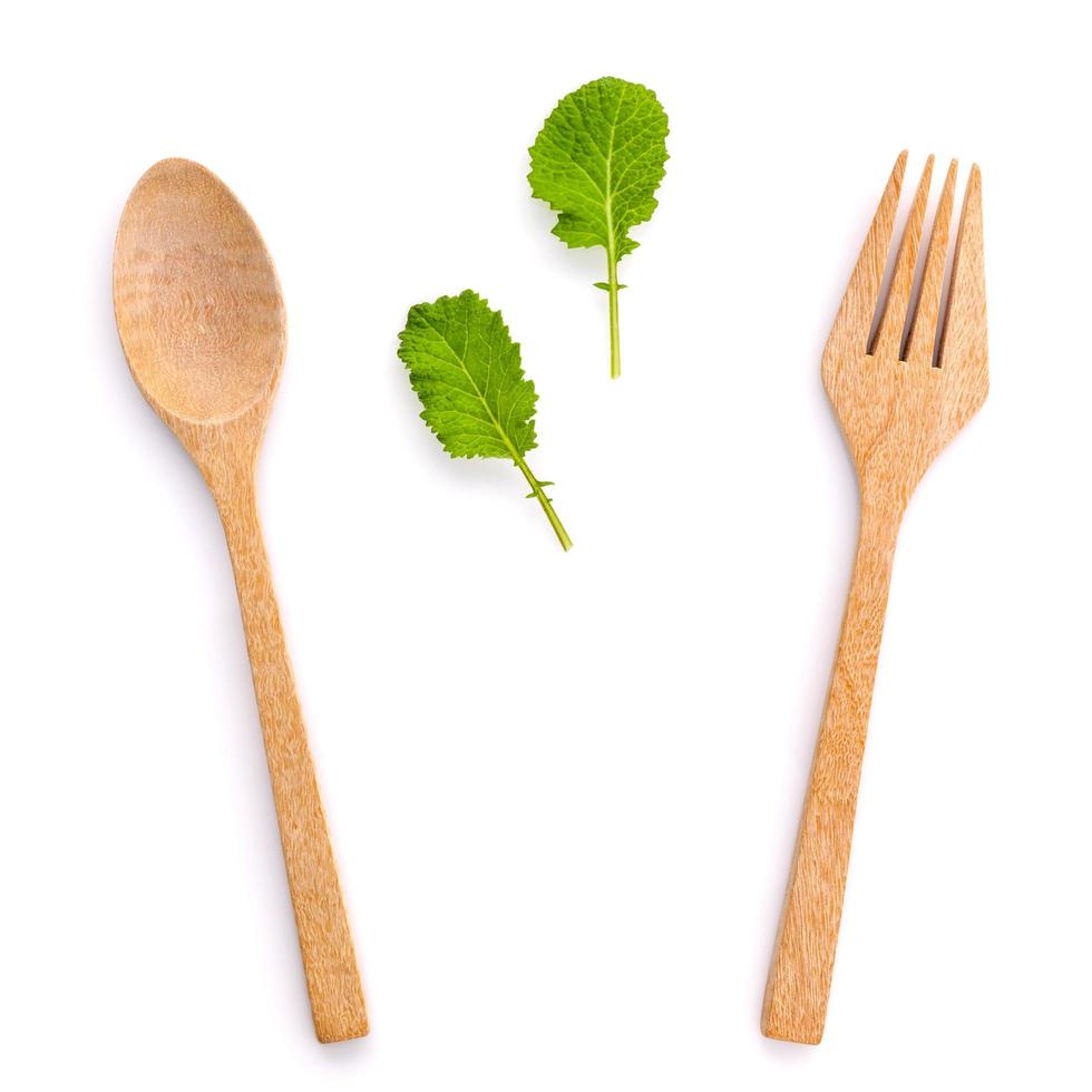 hojas verdes con cuchara de madera y tenedor sobre blanco foto