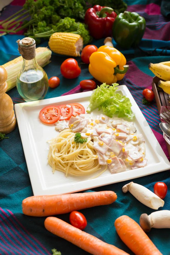 Pasta carbonara con tocino y parmesano en un plato blanco con verduras sobre un mantel de colores foto