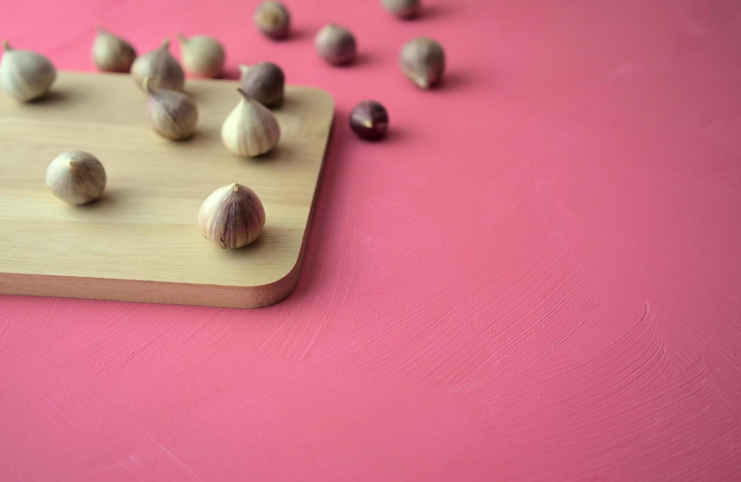 Garlic on cutting board on pink background photo