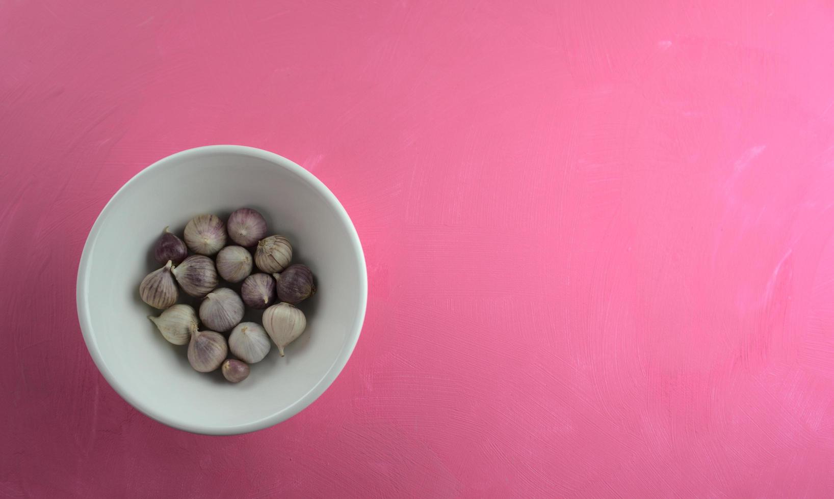 Ajo en un recipiente sobre fondo rosa acrílico áspero foto