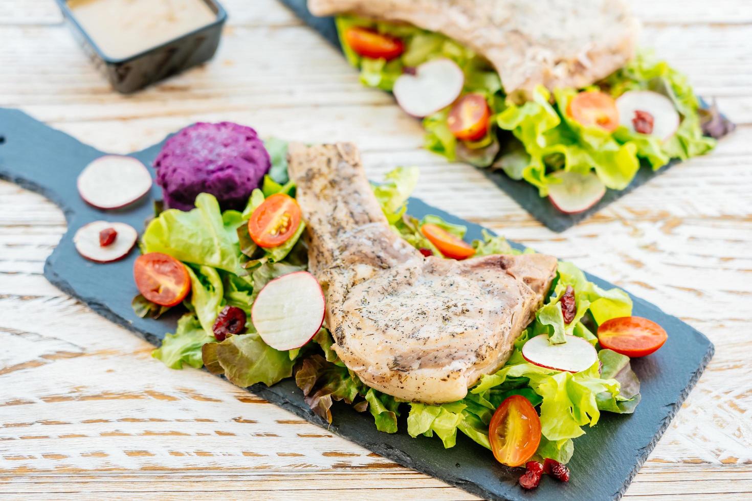 Grilled bbq pork chop meat steak on black plate with vegetables photo