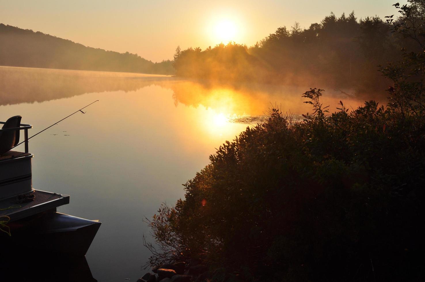 El sol se eleva sobre un lago brumoso con barco en el agua foto