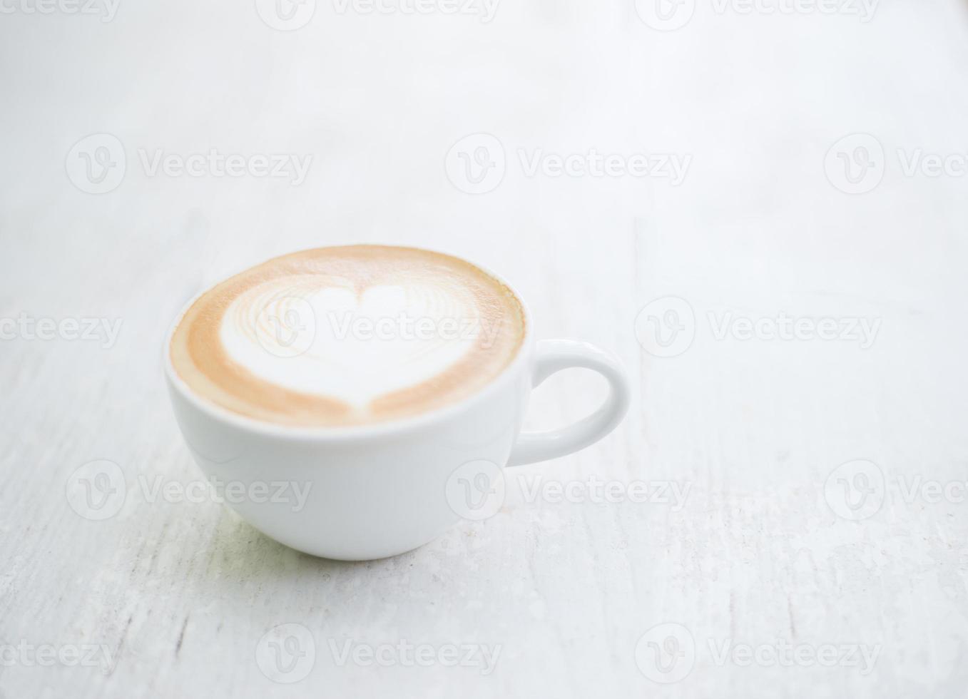 Cup of latte art heart shape coffee on white table photo