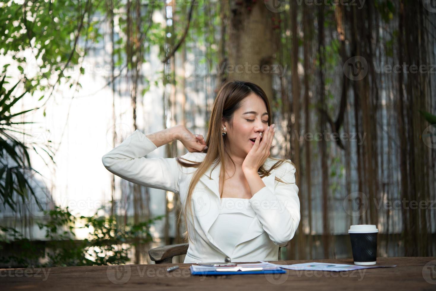 Young businesswoman stretching herself and yawning at workplace photo