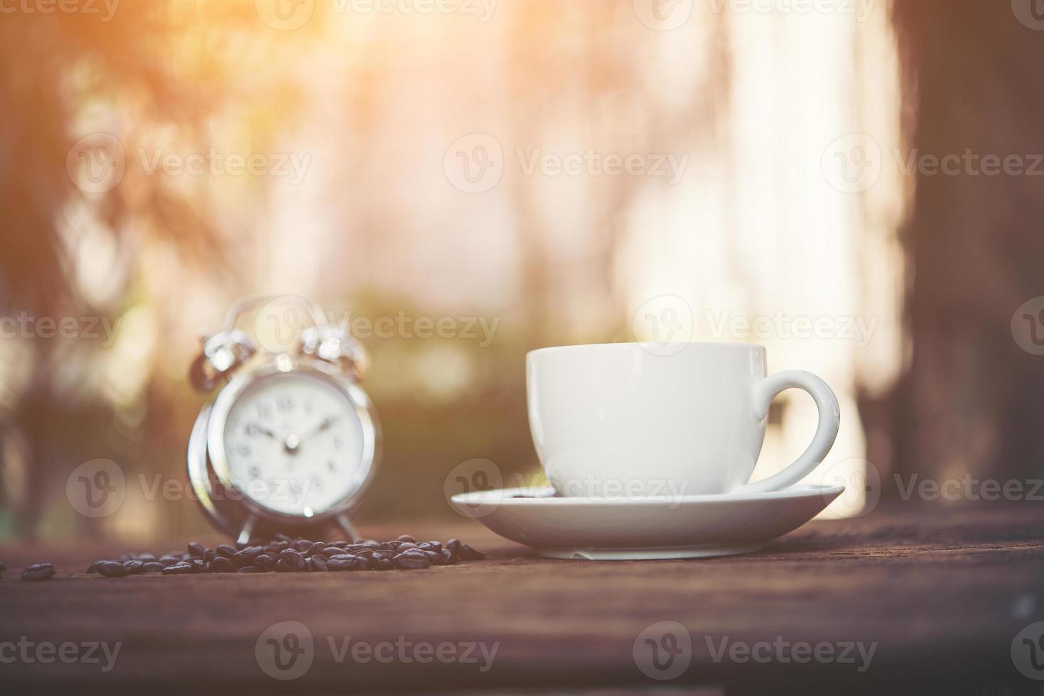 Cup of coffee with alarm clock on natural morning background photo