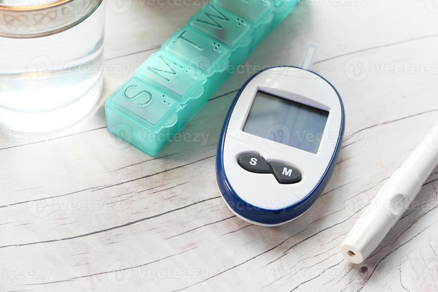 medidor de glucosa en sangre, pastillero y vaso de agua en la mesa foto