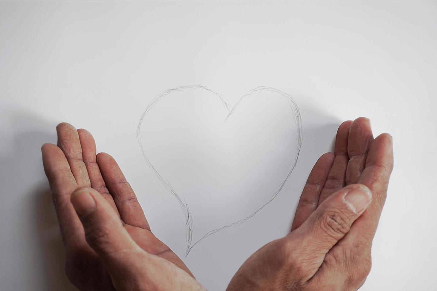 La mano de un joven cuidando una forma de corazón escrita a mano con un lápiz foto