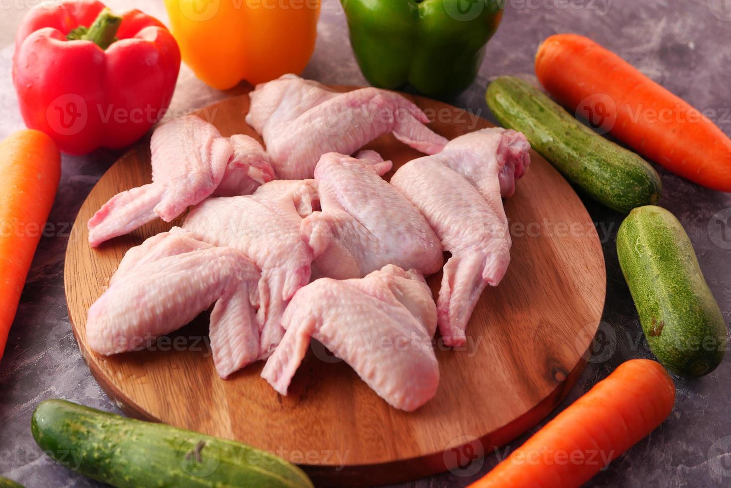 Raw chicken wings with vegetables on table photo