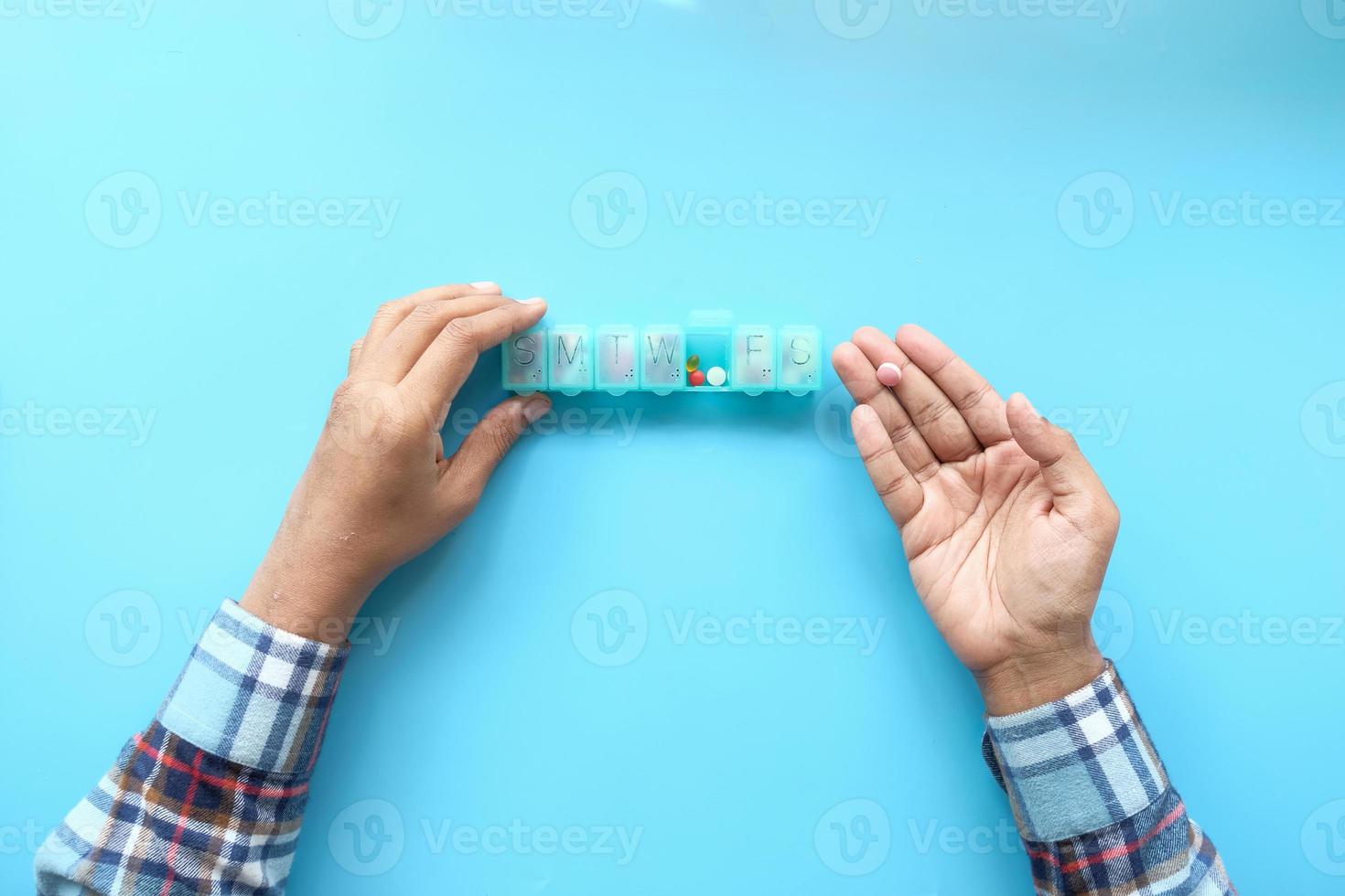 Vista superior de las manos del hombre tomando la medicina de un pastillero foto