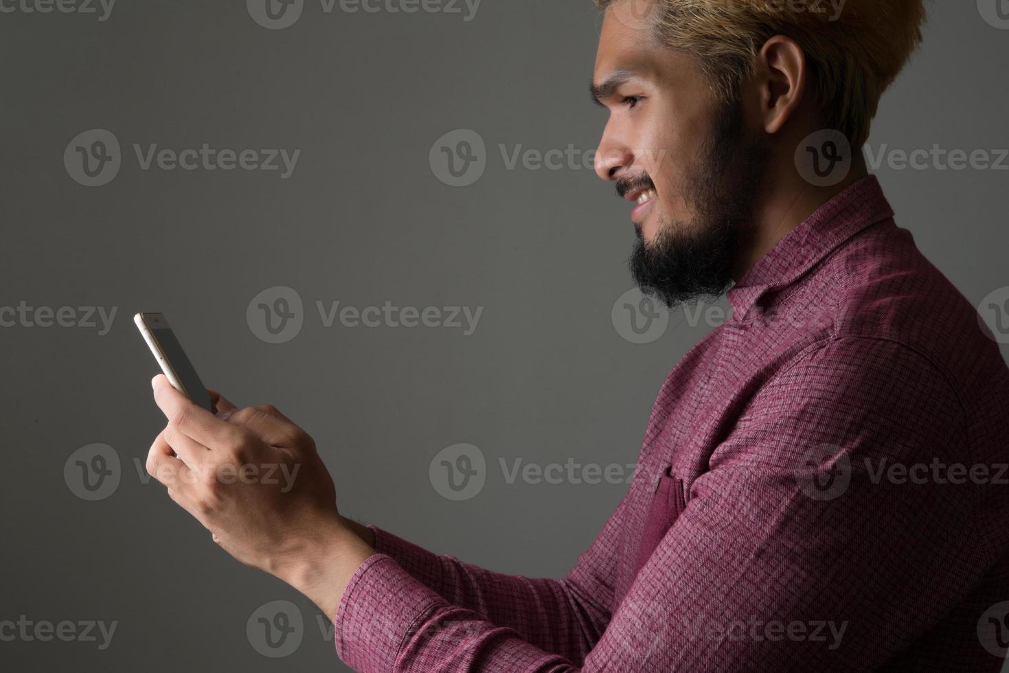 Handsome hipster man smiling while using smartphone isolated on black background photo