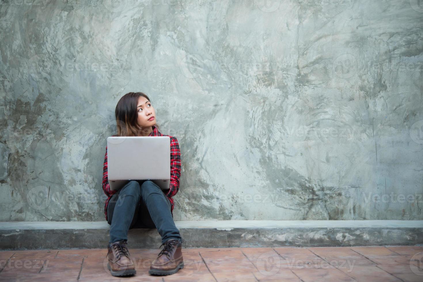 Happy young hipster woman using her laptop while sitting on the ground photo