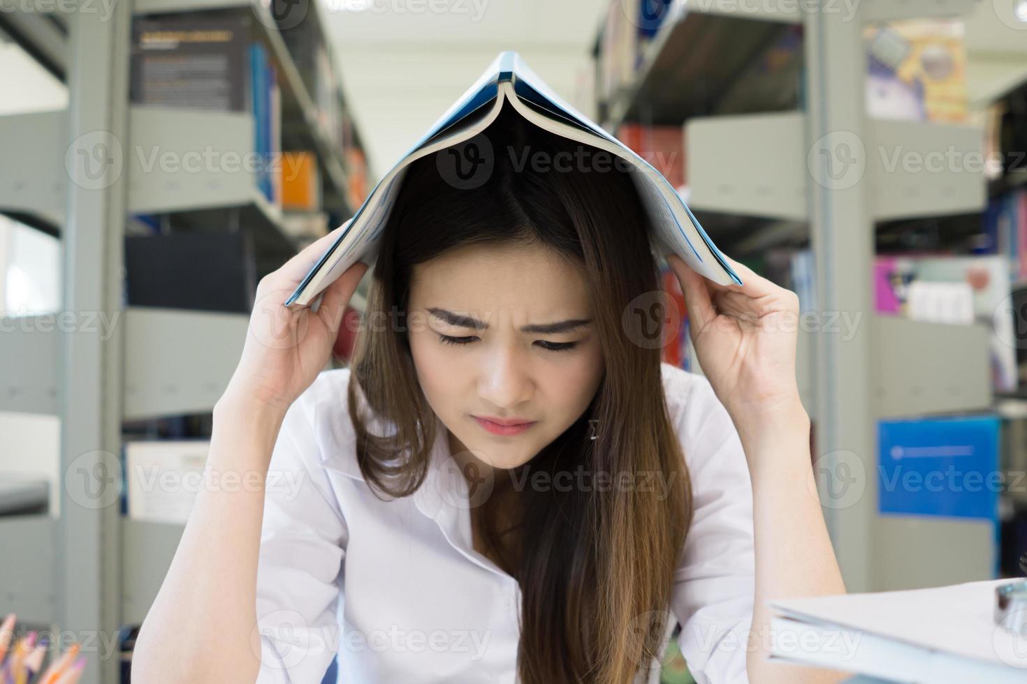 Retrato de estudiante que cubre su cabeza con un libro mientras lee foto