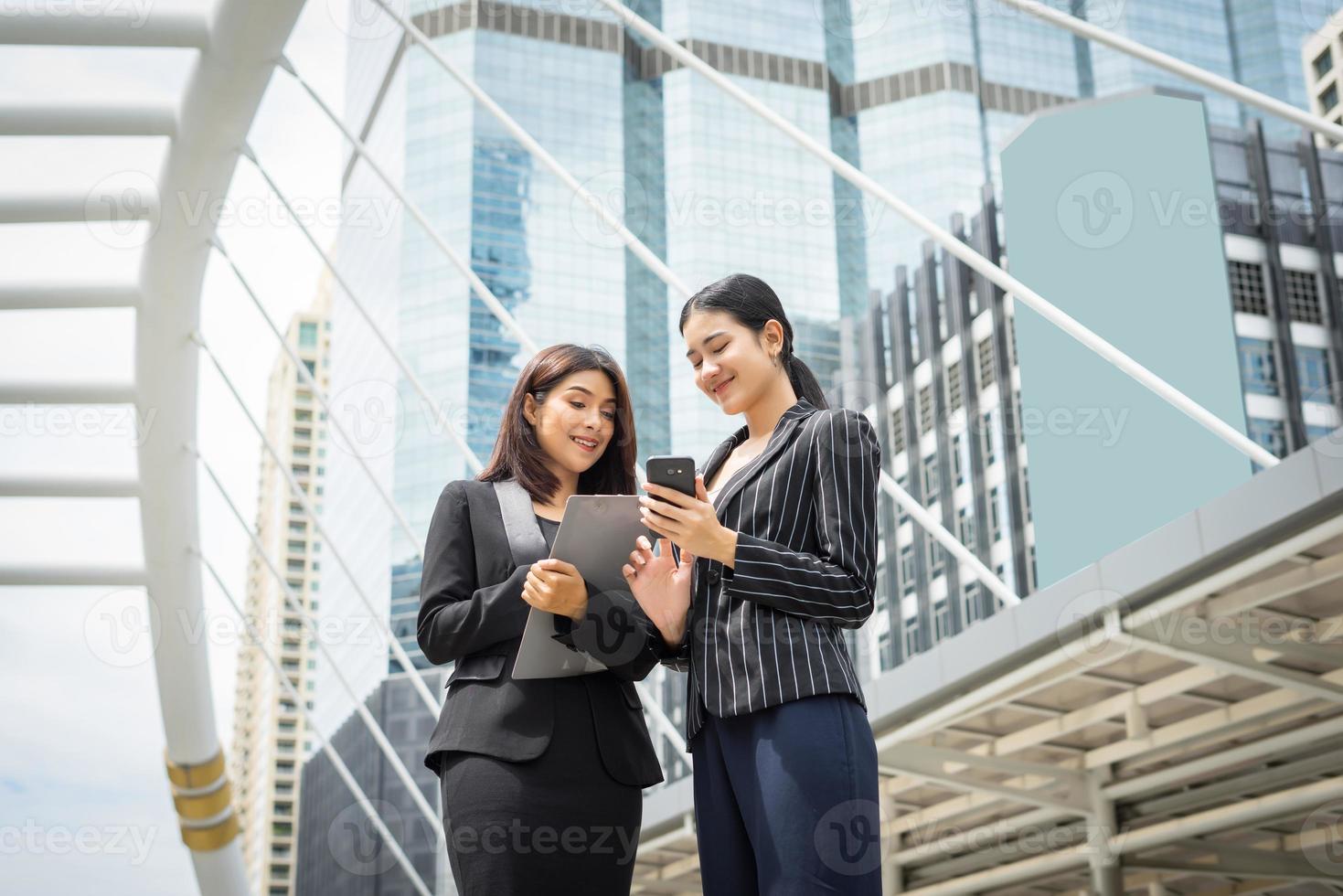 Dos mujeres de negocios usando un teléfono inteligente y discutiendo el trabajo en frente de la oficina foto