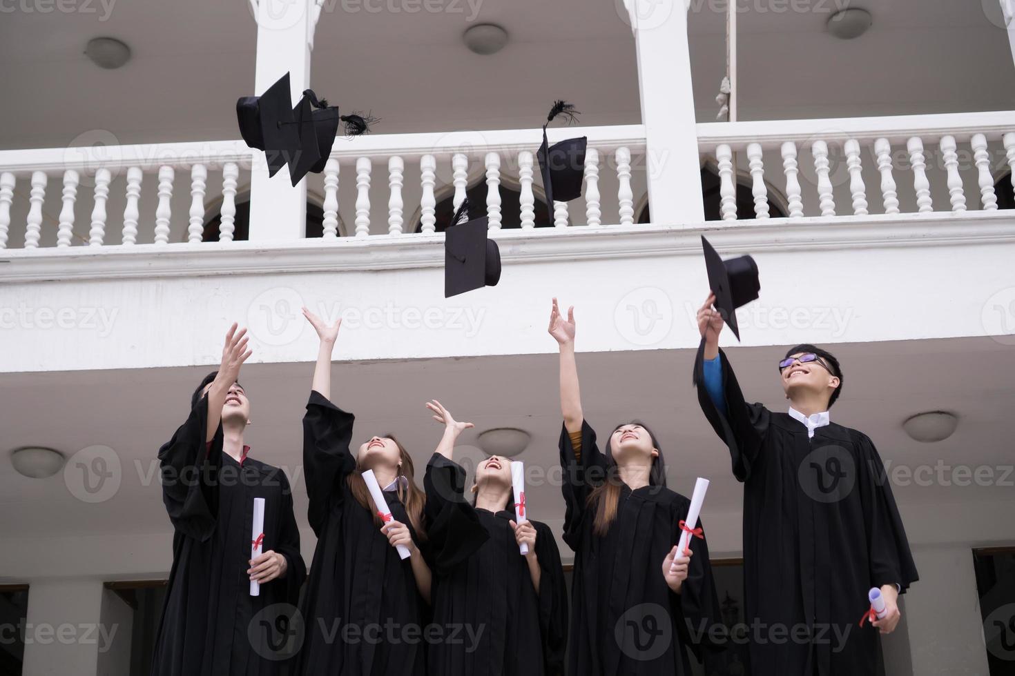 grupo de estudiantes exitosos lanzando sombreros de graduación al aire y celebrando foto