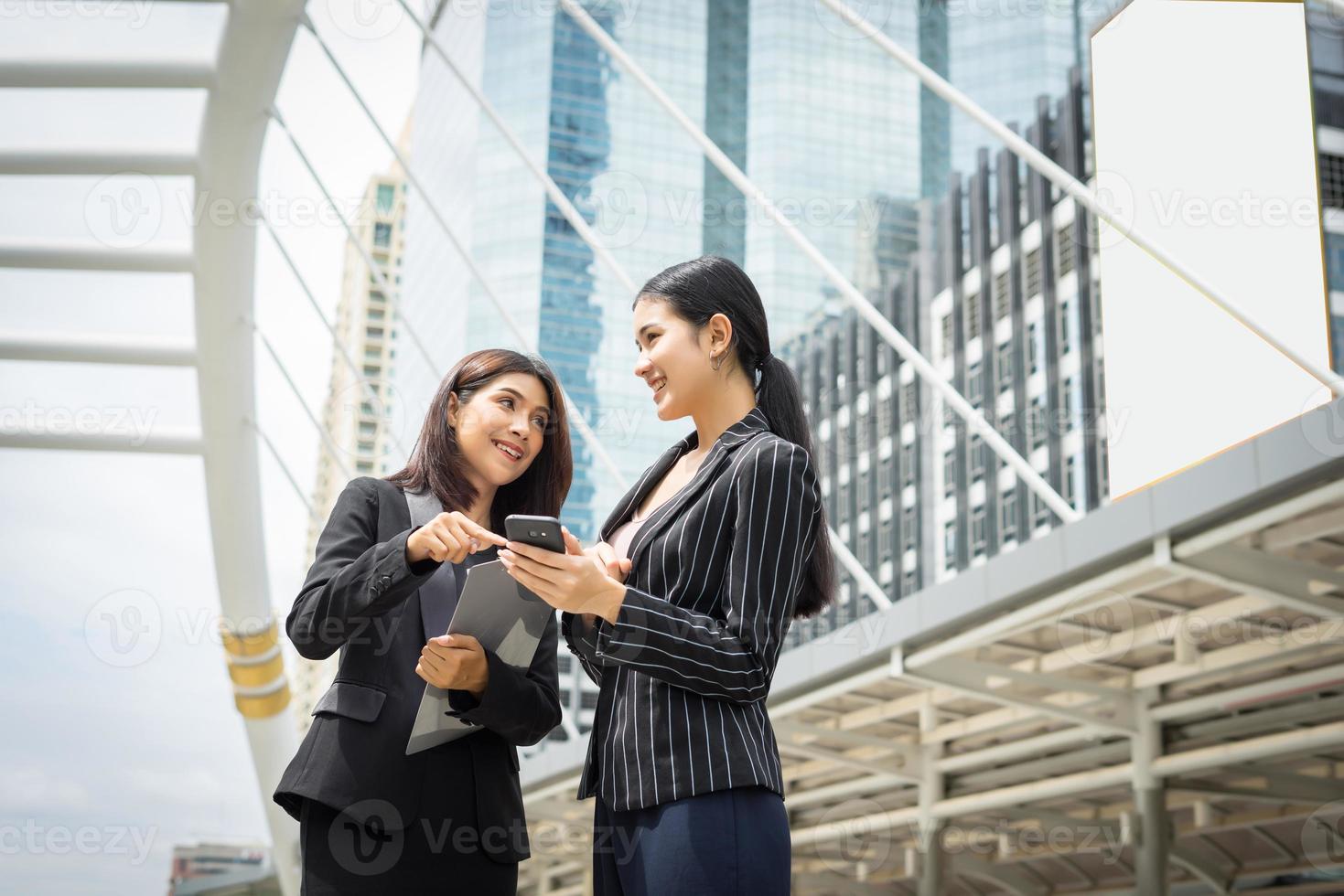 Two business woman using a smartphone and discussing work in front of the office photo