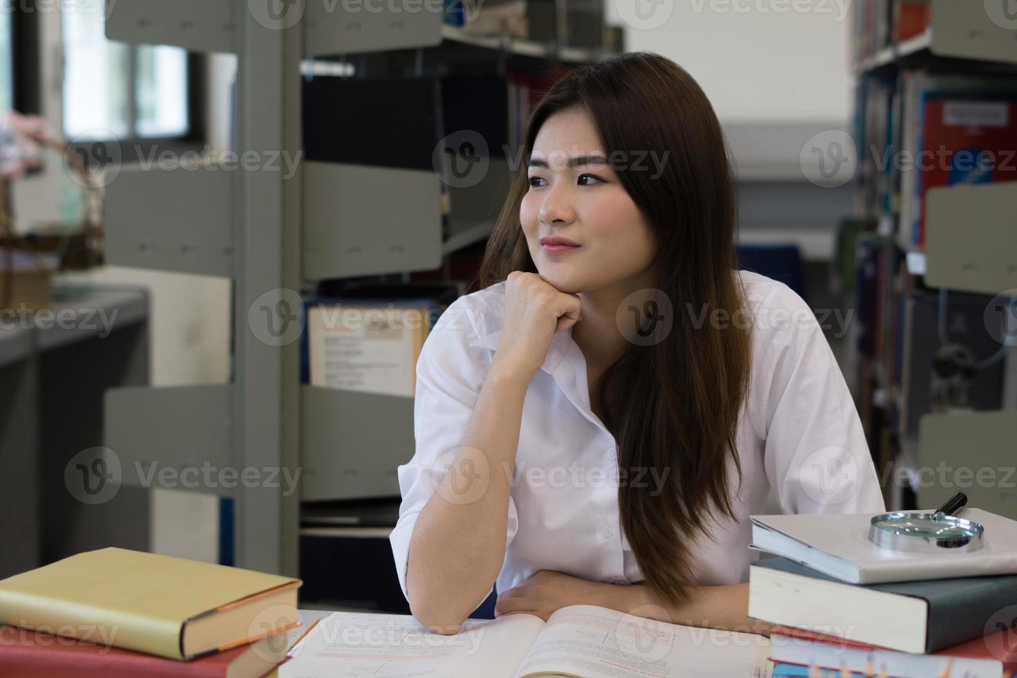 Joven estudiante bastante asiático sonriendo mientras lee en la biblioteca foto