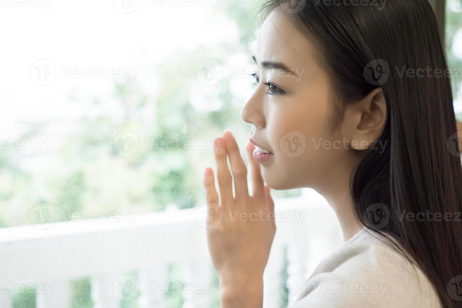 Mujer hermosa joven de pie junto a la ventana en casa foto