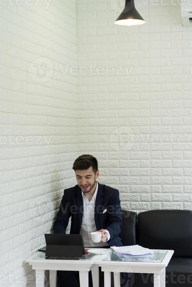 Joven empresario tomando un café trabajando en un portátil foto