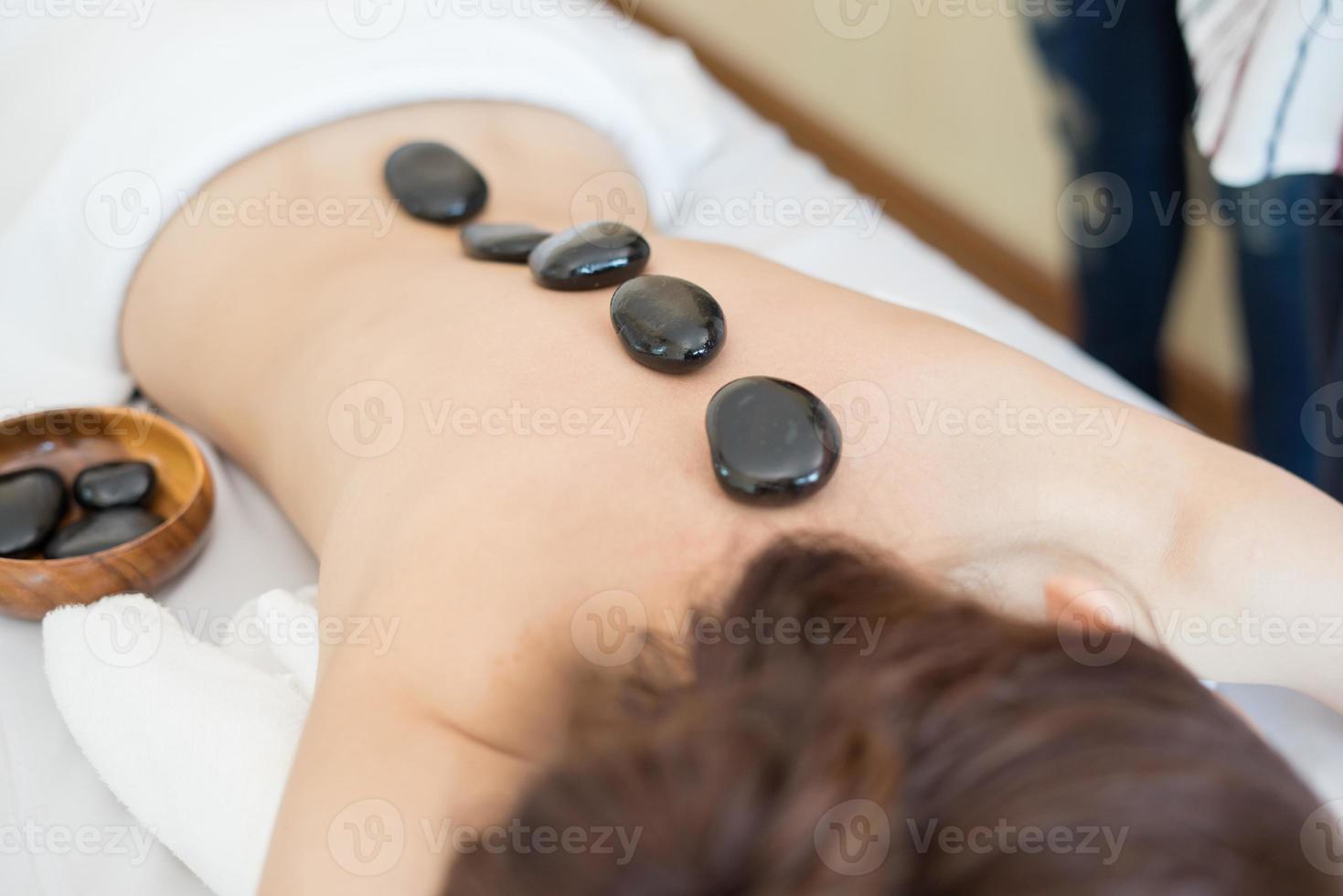 Hermosa joven recibiendo masaje con piedras calientes en el salón spa foto