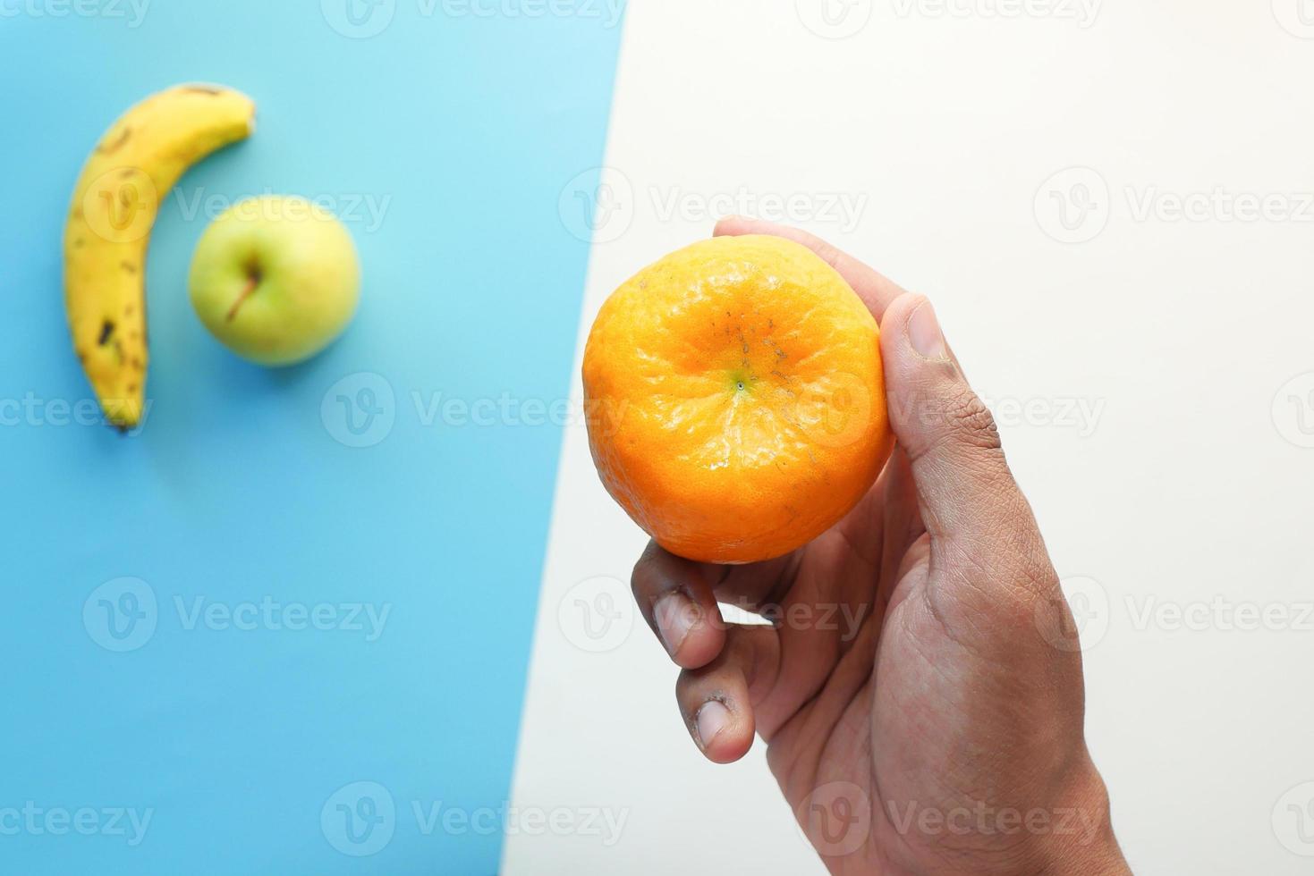Mano sujetando fruta naranja madura sobre fondo azul. foto