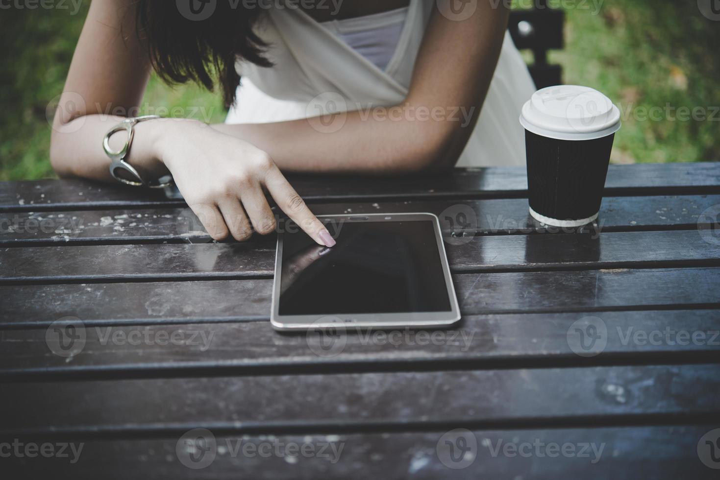 Close-up of woman holding tablet computer on wooden table with cup of coffee photo