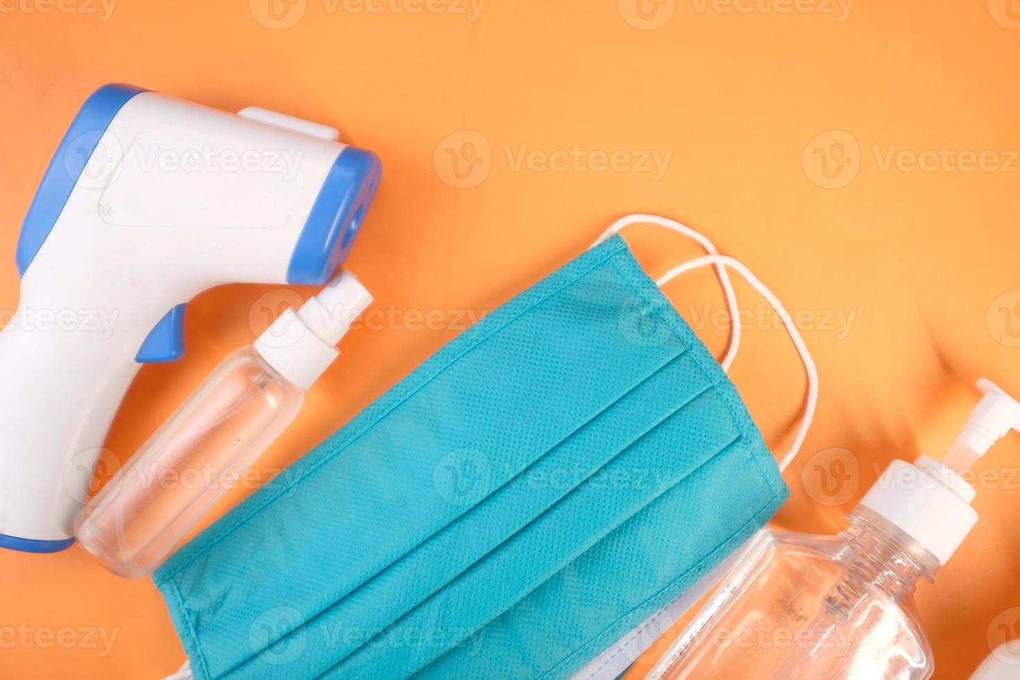 Surgical masks, thermometer, and hand sanitizer on orange background photo