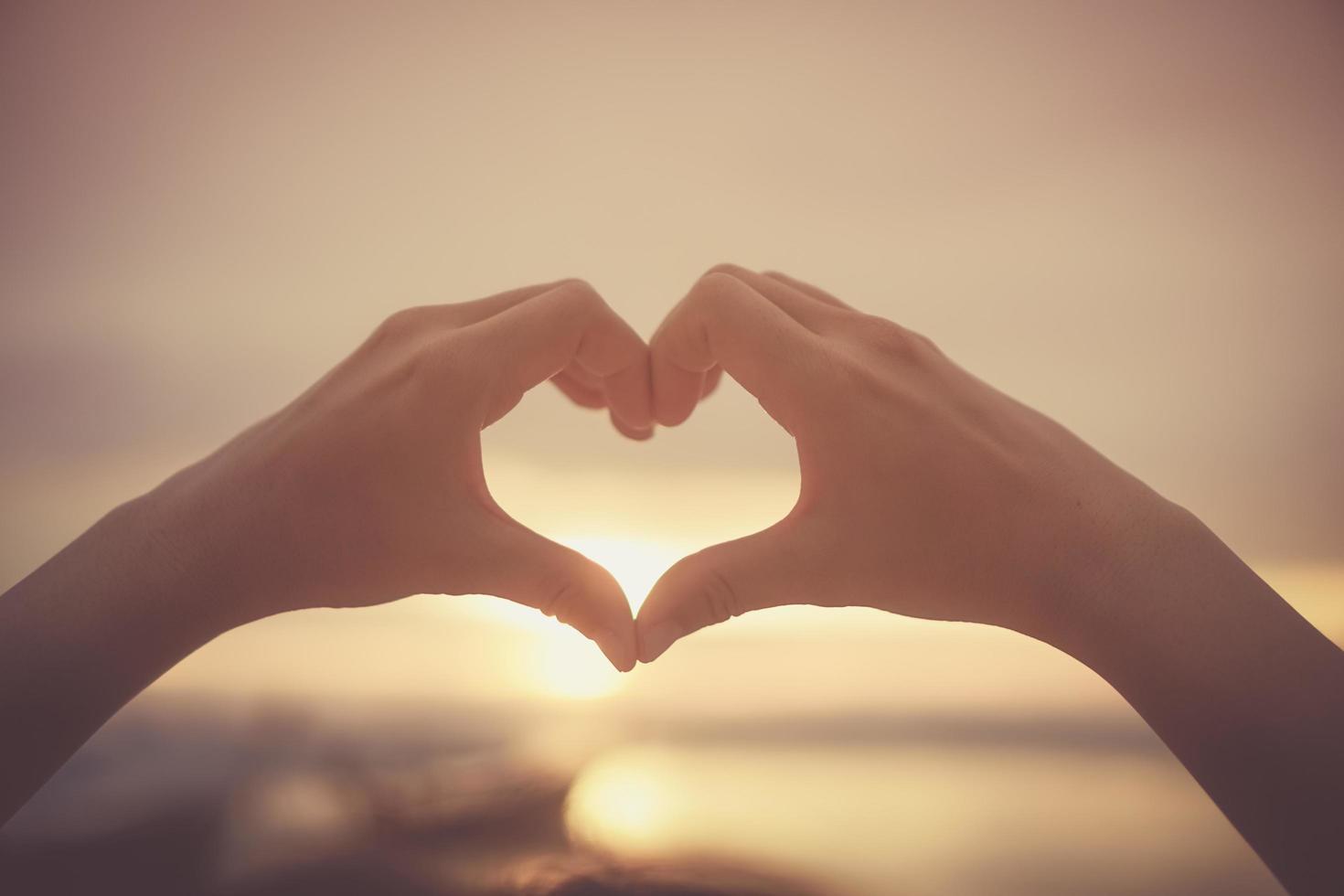 Manos de mujer haciendo forma de corazón en el cielo y el fondo bokeh foto