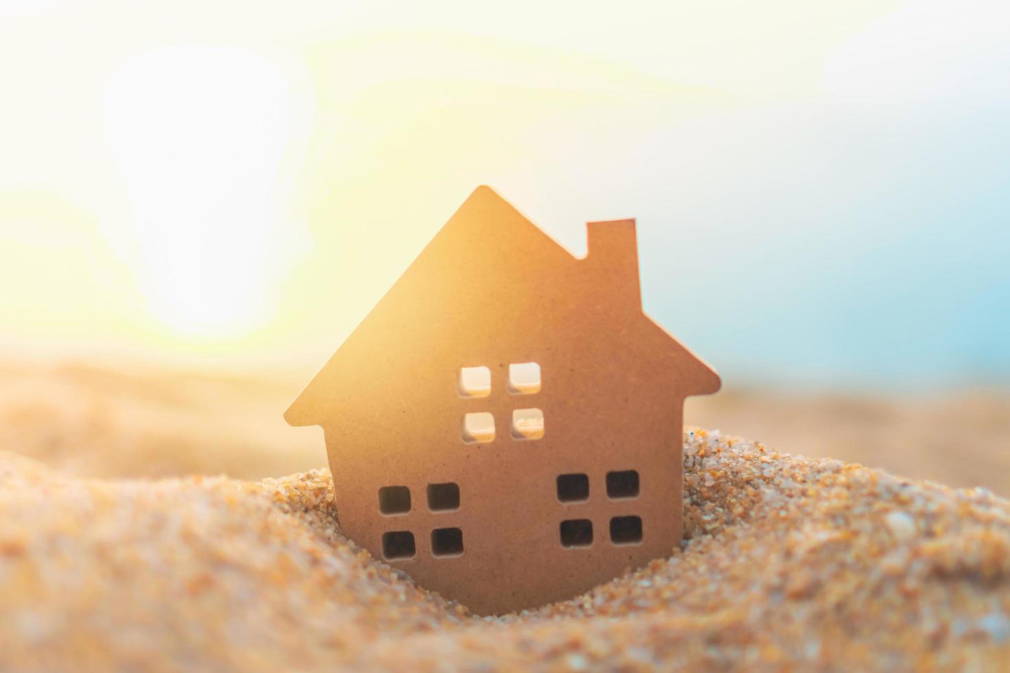 Close-up of tiny home model on the sand with sunlight background photo