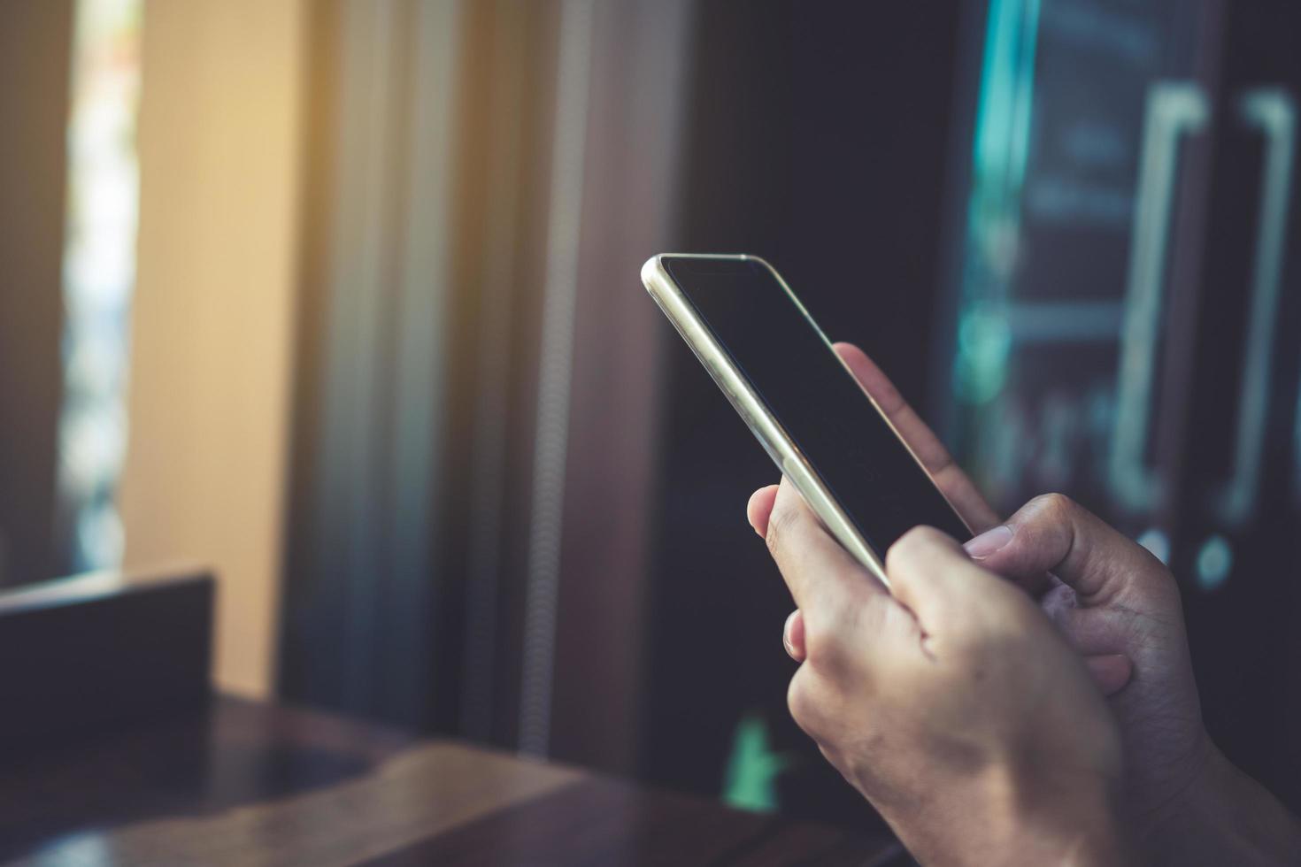 Mano de mujer con un teléfono inteligente y una computadora portátil con la luz del sol de la cafetería foto