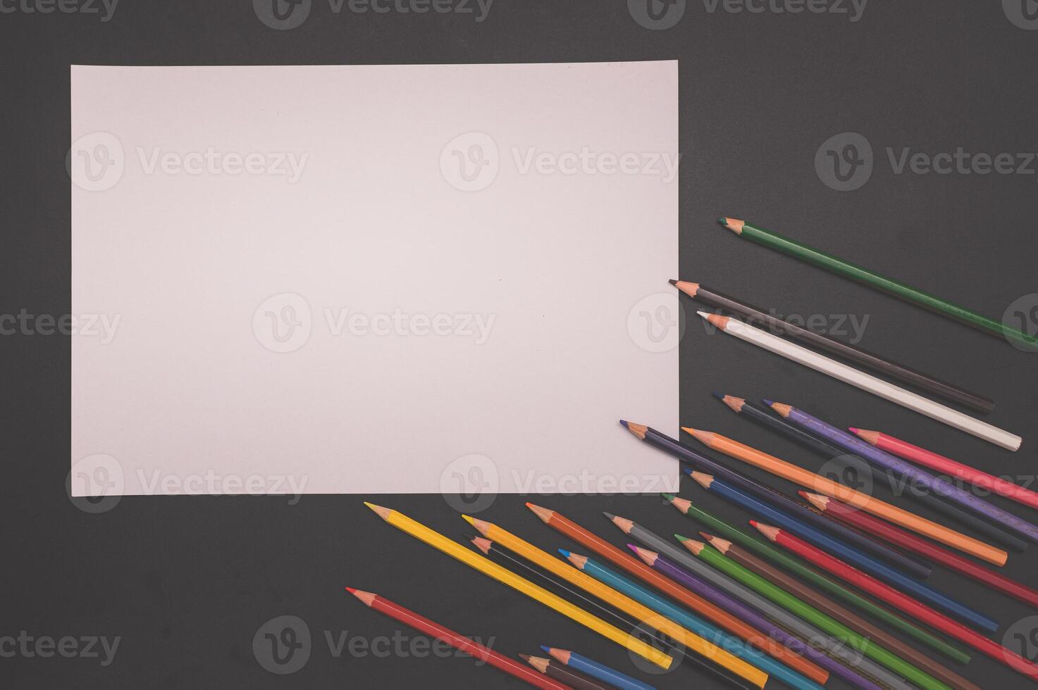A blank piece of paper surrounded by colored pencils photo