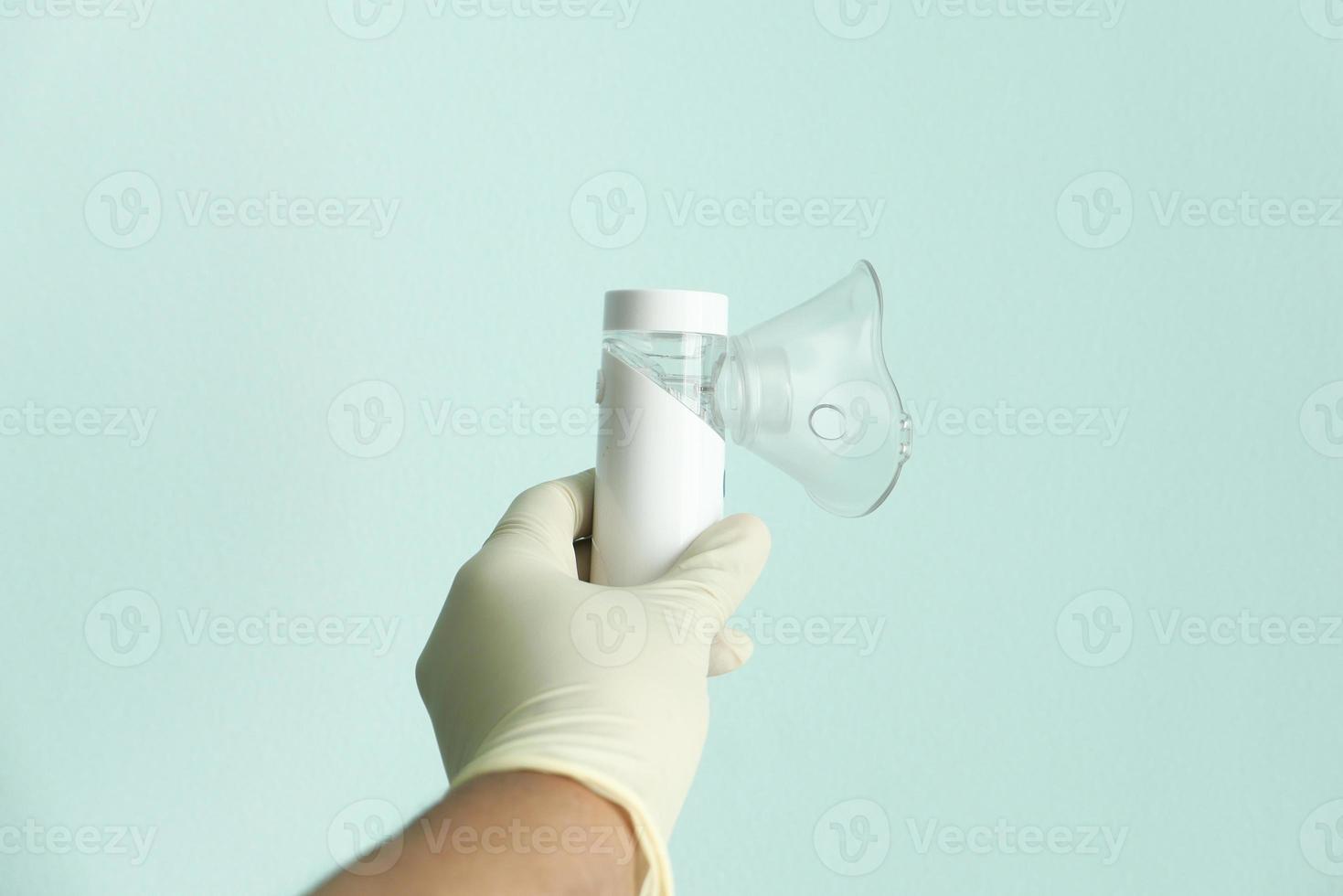 Hand in latex gloves holding a nebulizer on a light green background photo