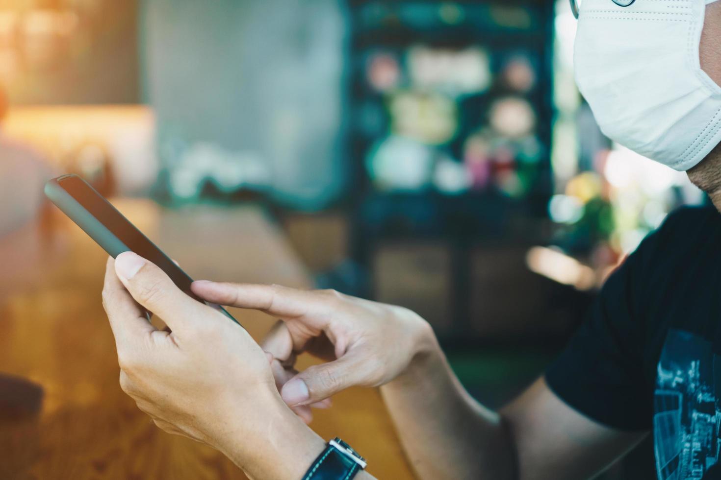 Man wearing a mask using a smartphone in public cafe photo