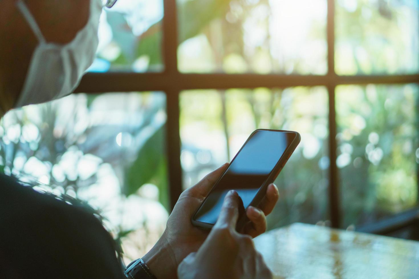 Hombre que llevaba una máscara con un teléfono inteligente en la cafetería pública foto