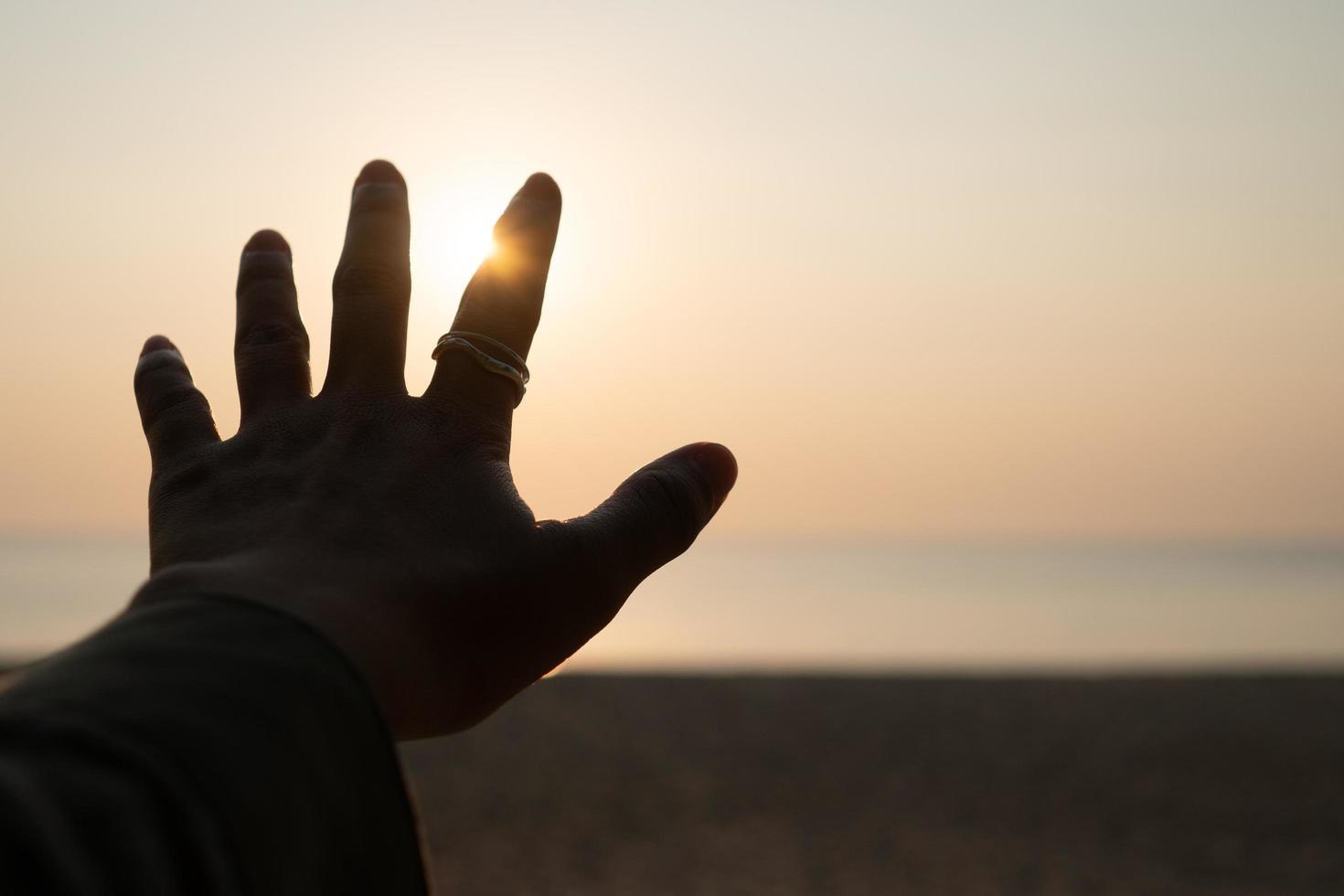 Mano extendiendo la mano al cielo del atardecer en la arena de la playa, fondo de naturaleza foto