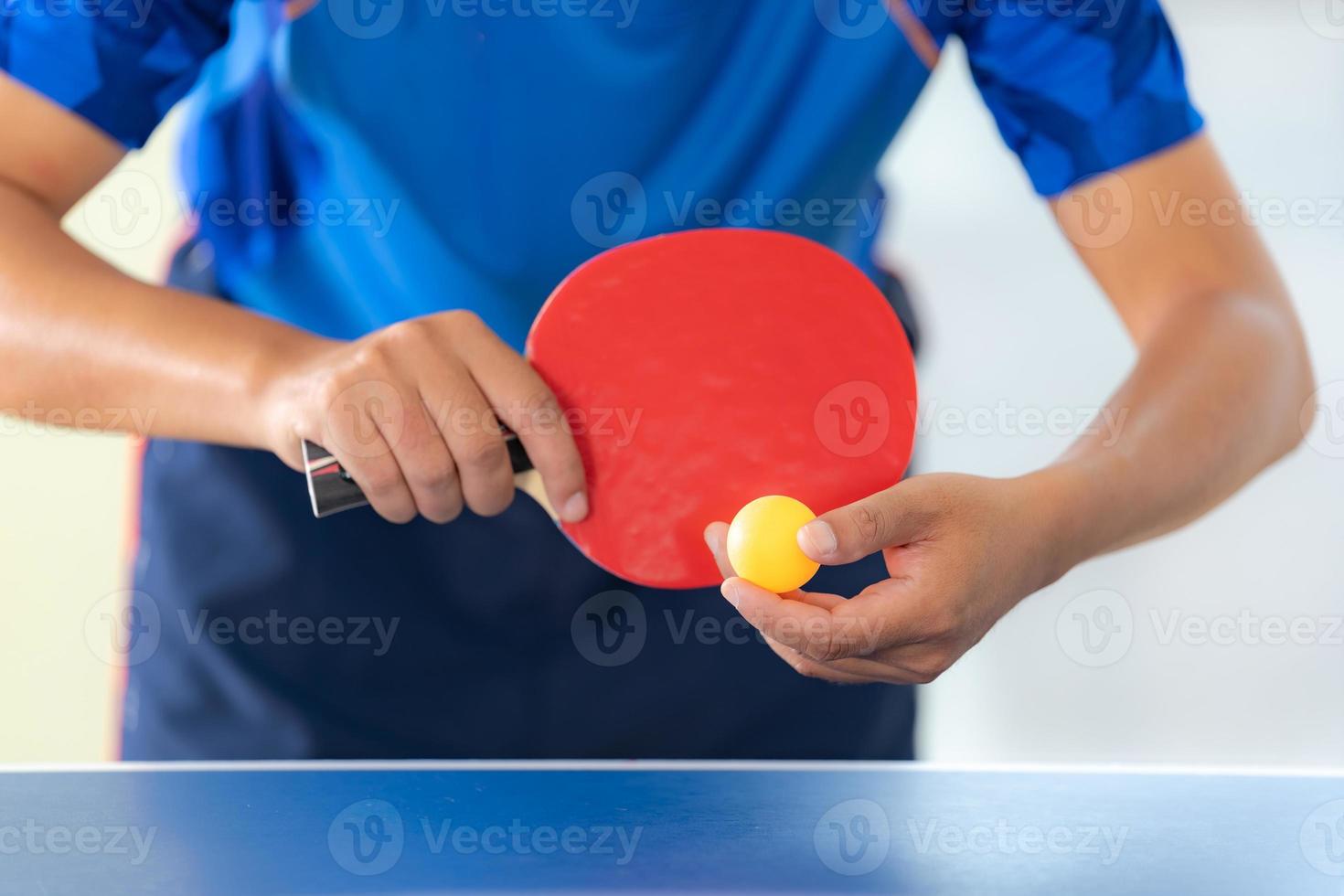 Macho jugando tenis de mesa con raqueta y pelota en un pabellón deportivo foto