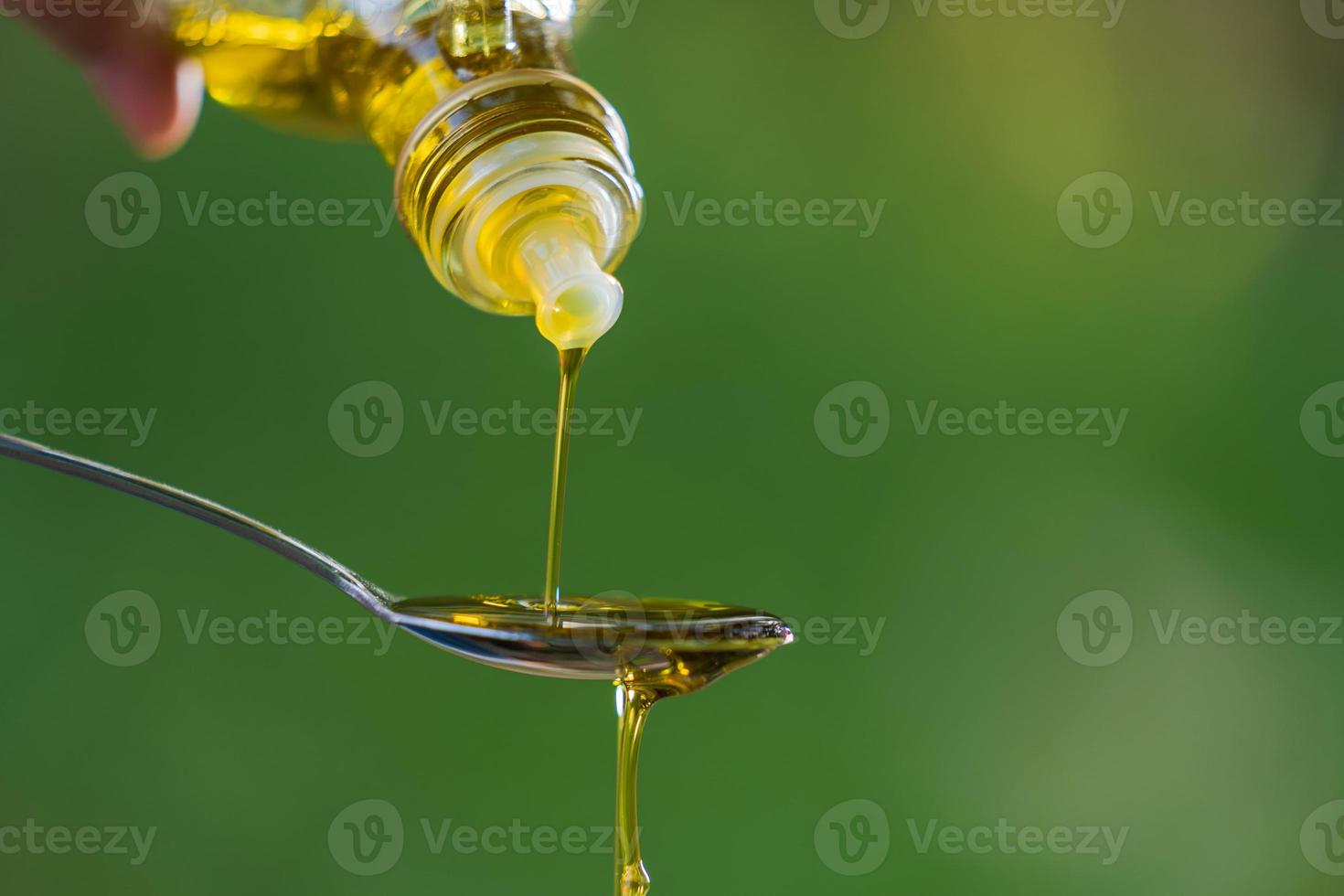 Verter el aceite de oliva en una cuchara en el fondo del jardín del parque verde foto