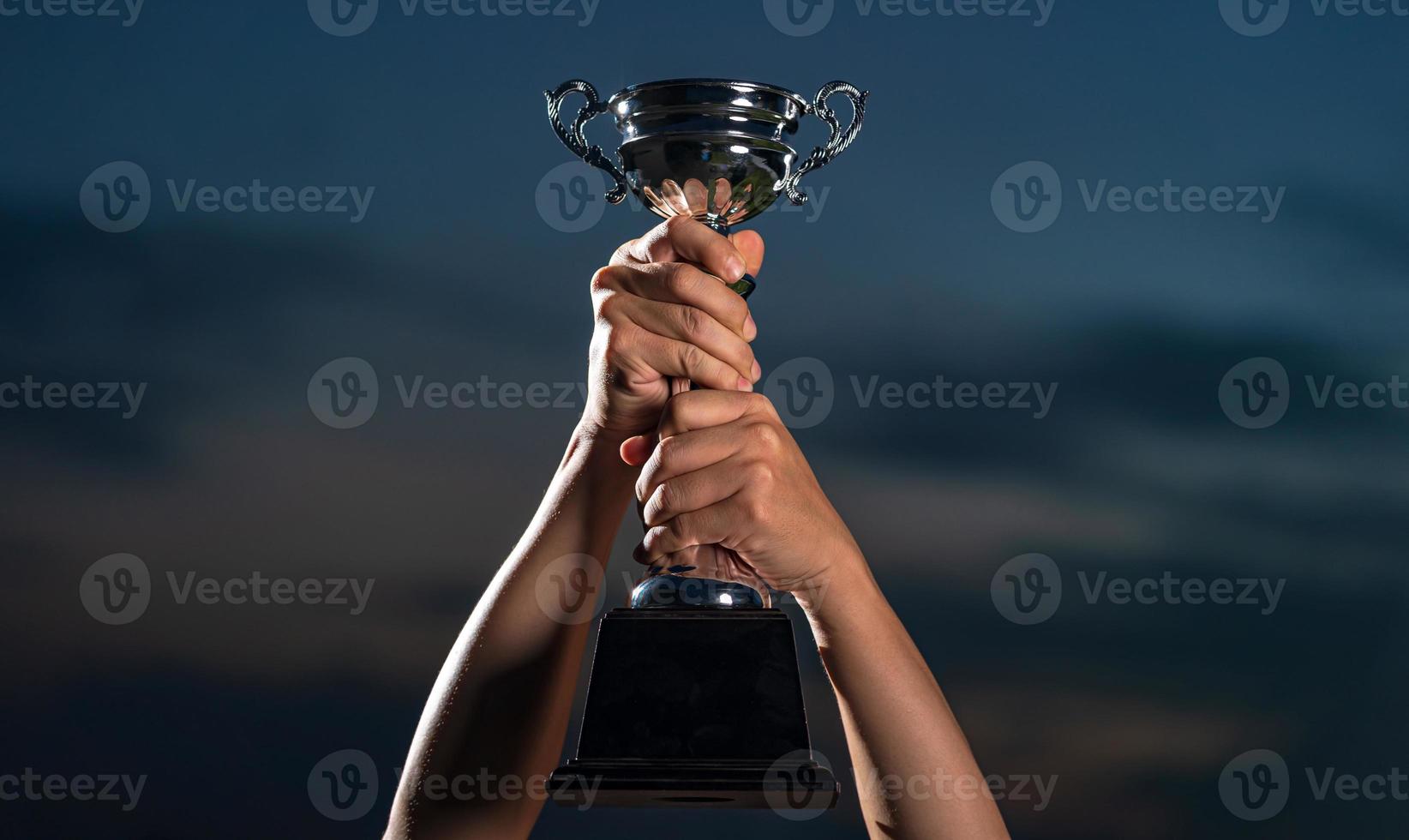 A man holding up a trophy cup on against cloudy twilight sky background photo