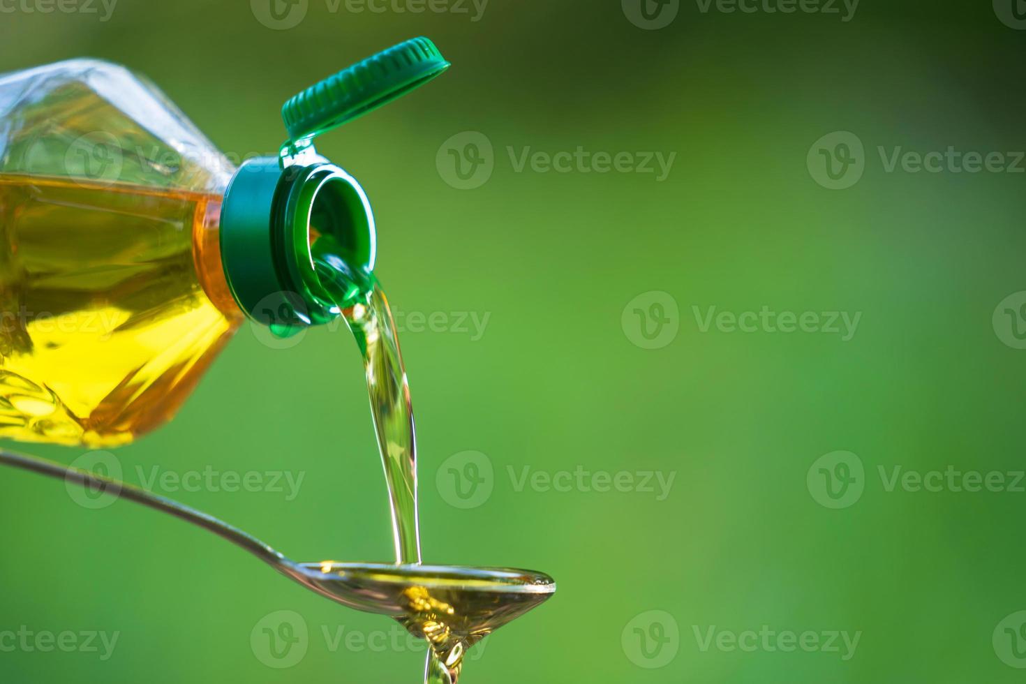 Mano vertiendo aceite vegetal de botella a cuchara foto