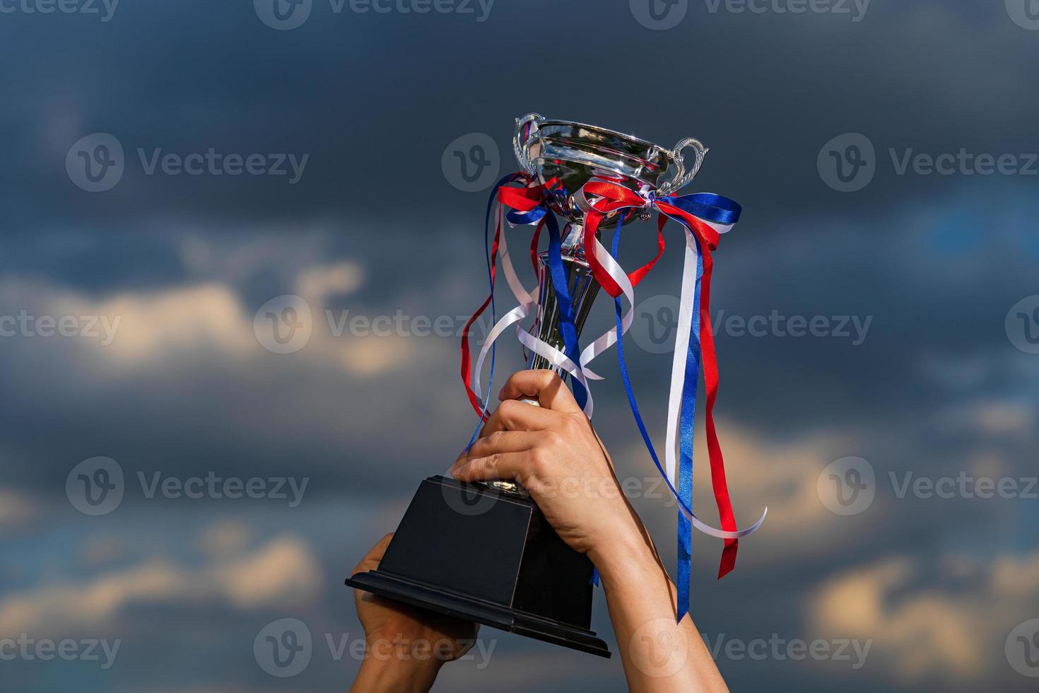 A man holding up a trophy cup on against cloudy twilight sky background photo