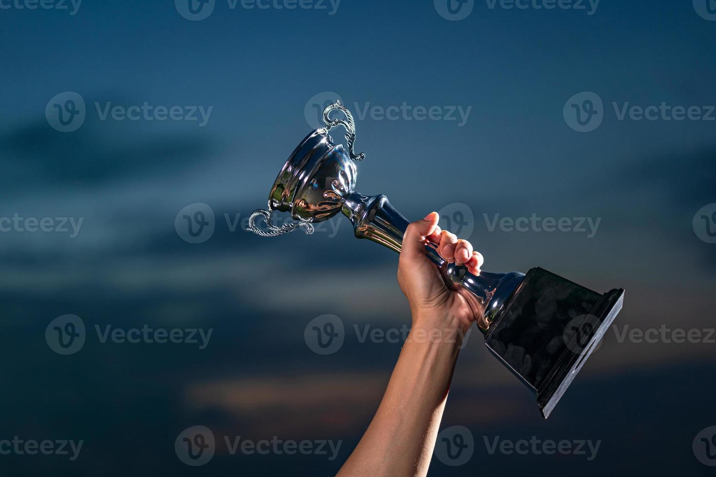 A man holding up a trophy cup on against cloudy twilight sky background photo