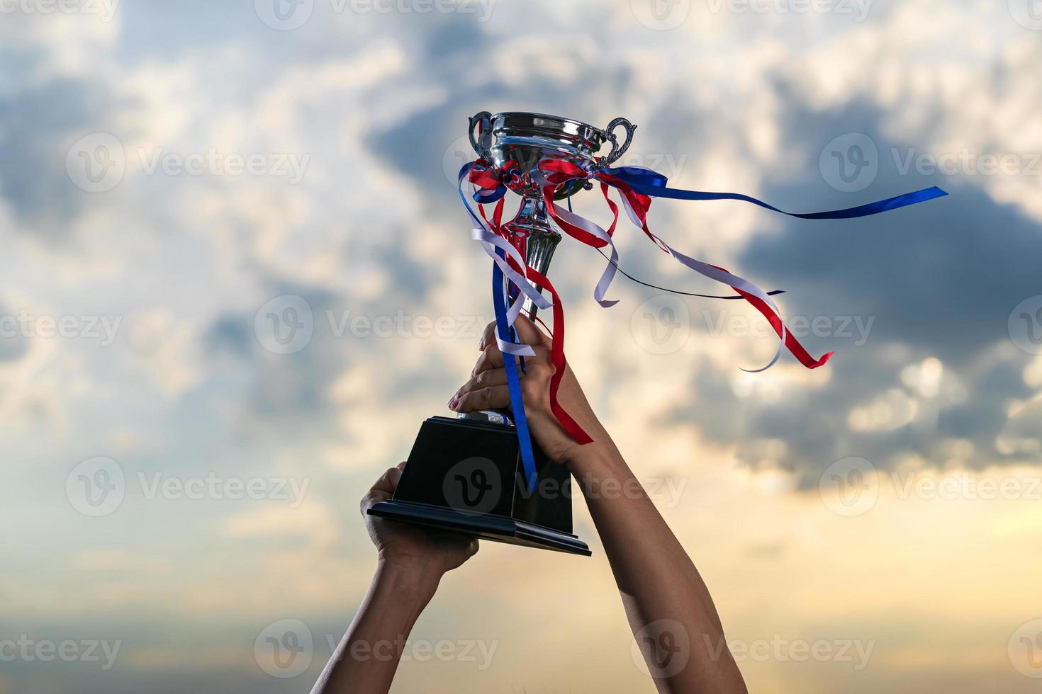 A man holding up a trophy cup on against cloudy twilight sky background photo