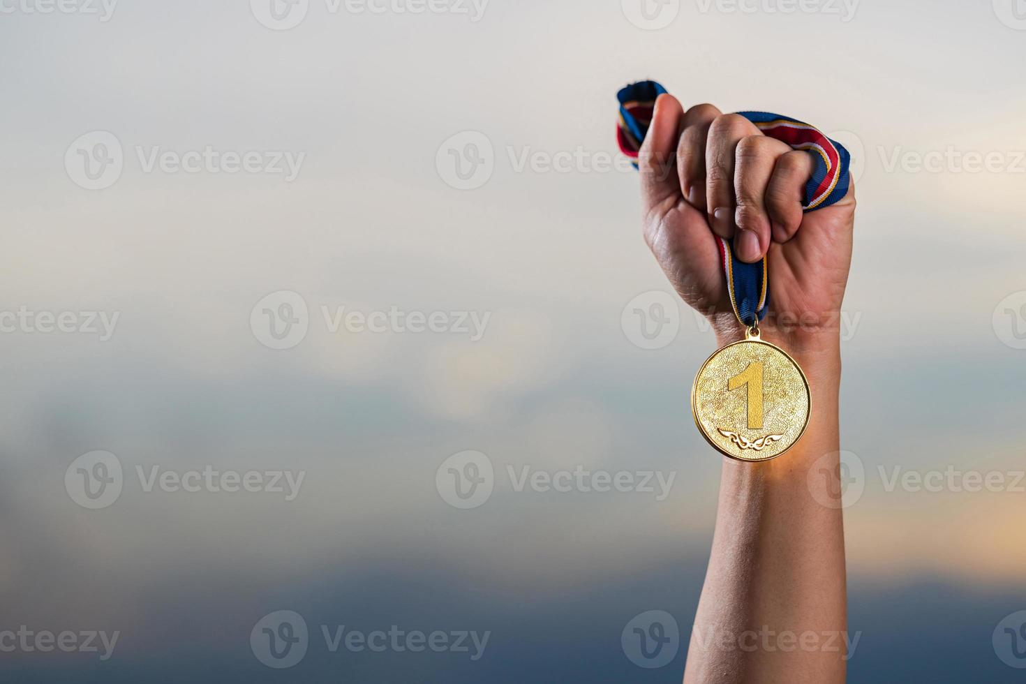 Mano sujetando la medalla de oro contra el fondo del cielo crepuscular nublado foto