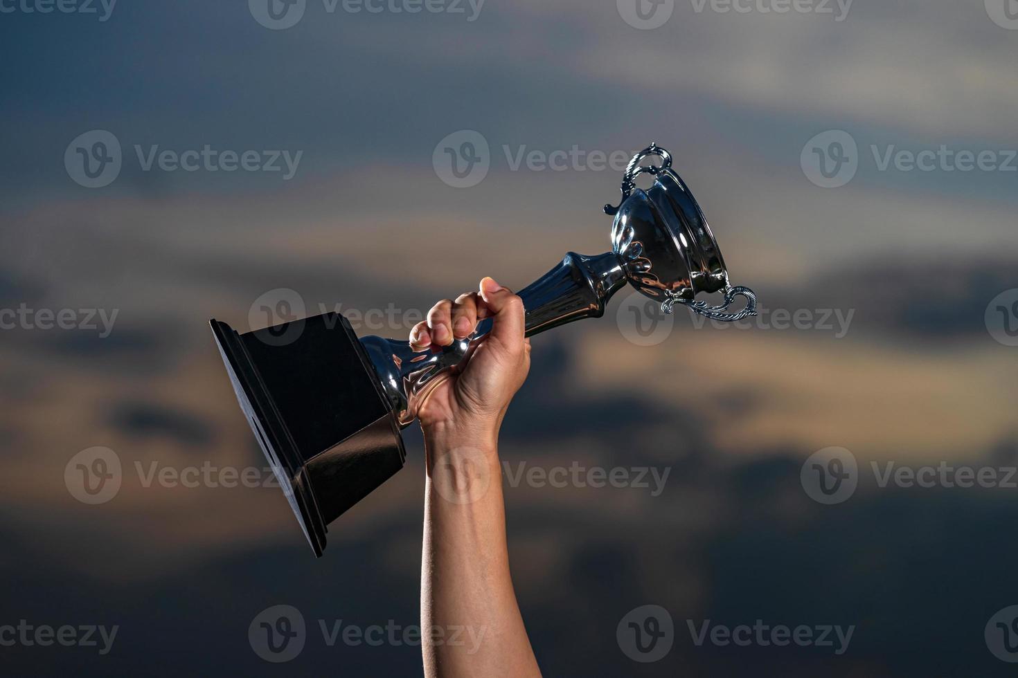 A man holding up a trophy cup on against cloudy twilight sky background photo
